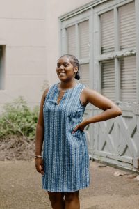 A teen stands in a courtyard wearing a blue striped top smiles and looks to the distance