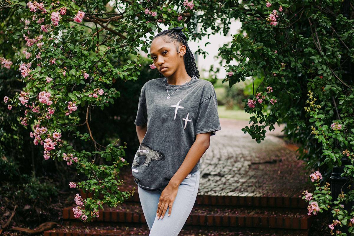 A teen poses outside under a pink flowering tree