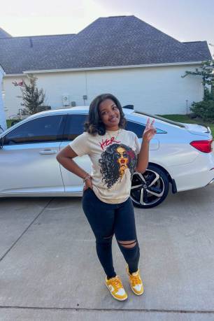 A young lady smiles for a photo on first day of school standing in front of a white car