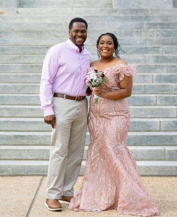 A teen in a peach formal dress poses beside her father outside