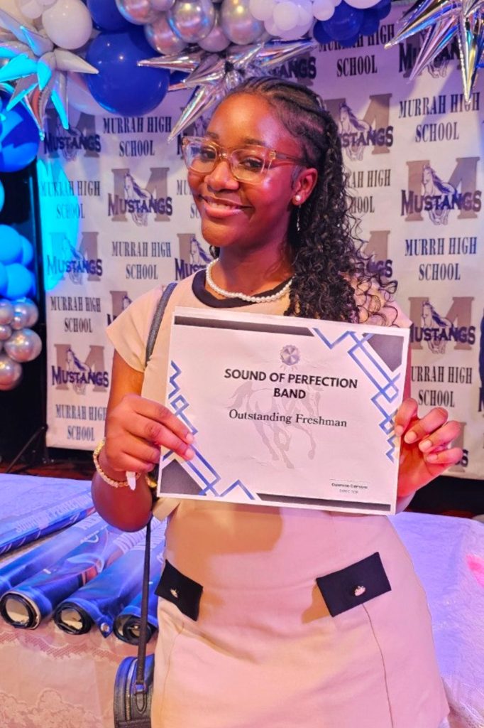 Young Black woman smiling while holding an award.