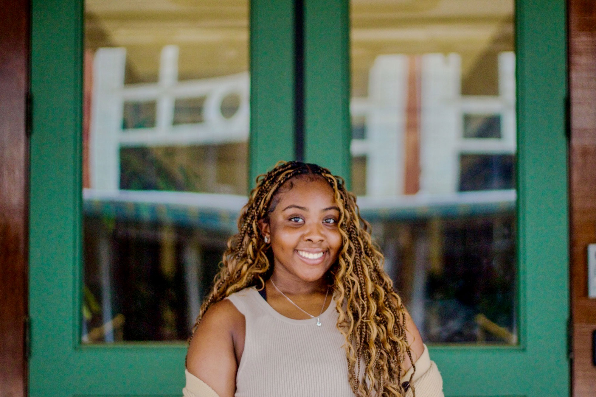 A teen with long hair stands outside a pair of green glass doors