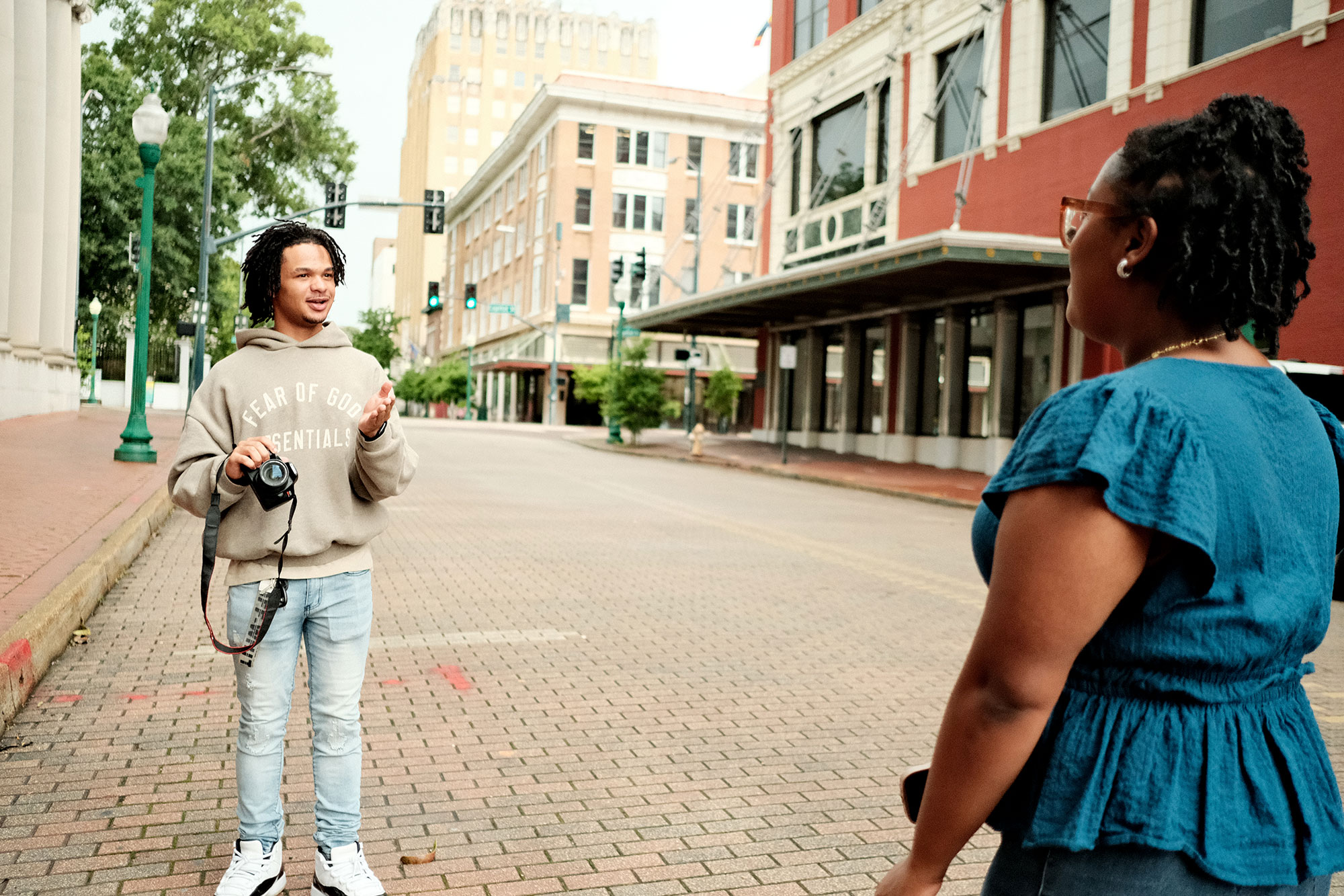 A boy and girl stand on a brick paved street, taking photos