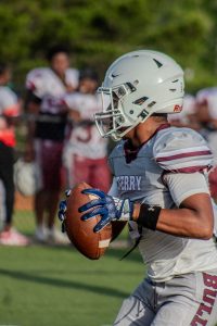A young man in a light grey and maroon football uniform with ball in hand