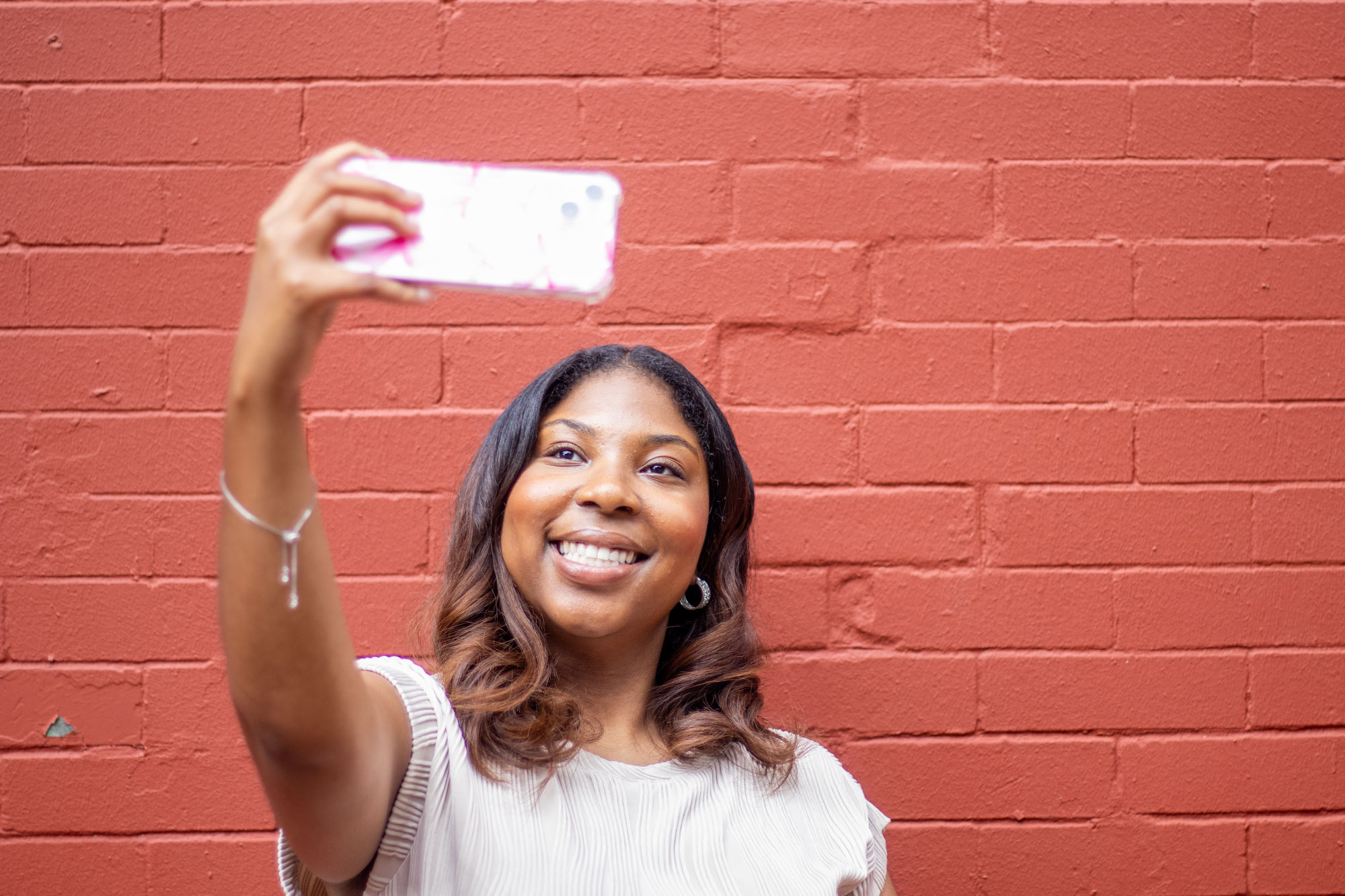 A teen takes a selfie against a red painted brick wall