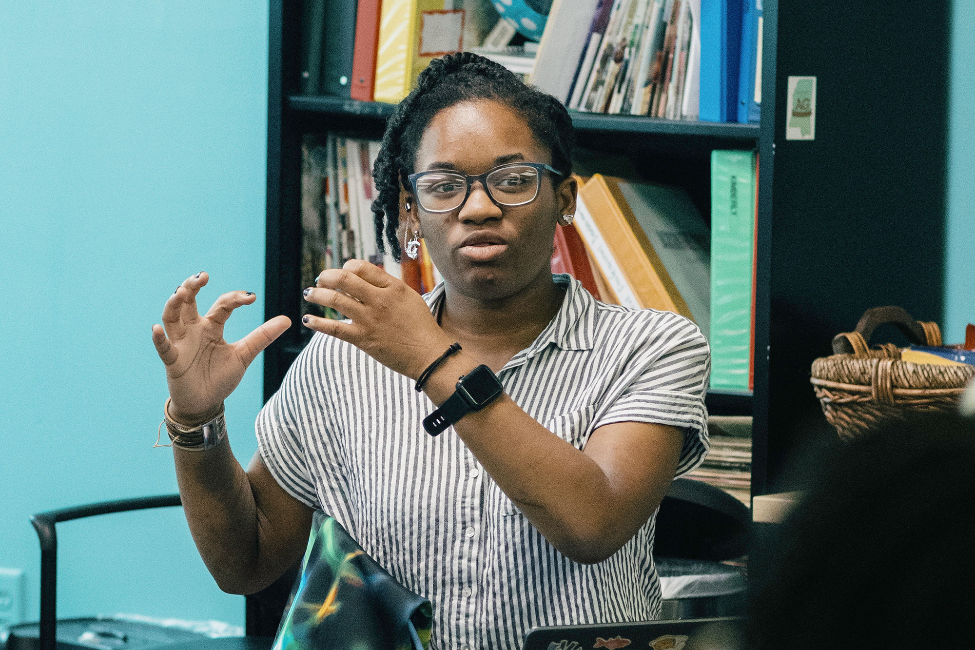 A teen in a stripped top and glasses gestures with their hands while talking