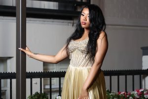Madison Ford posing and leaning on a pole in a gold prom dress