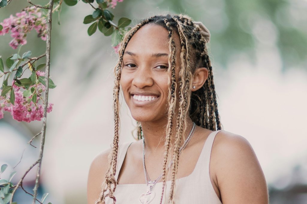 A teen with long honey braids stands outside beside a pink floral vine