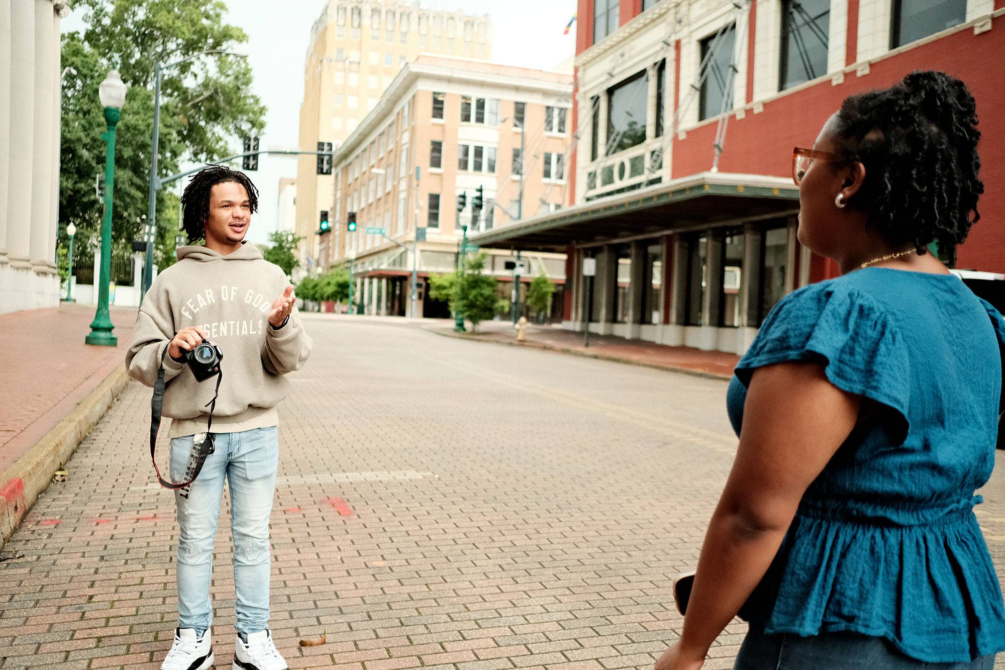 A boy and girl stand on a brick paved street, taking photos