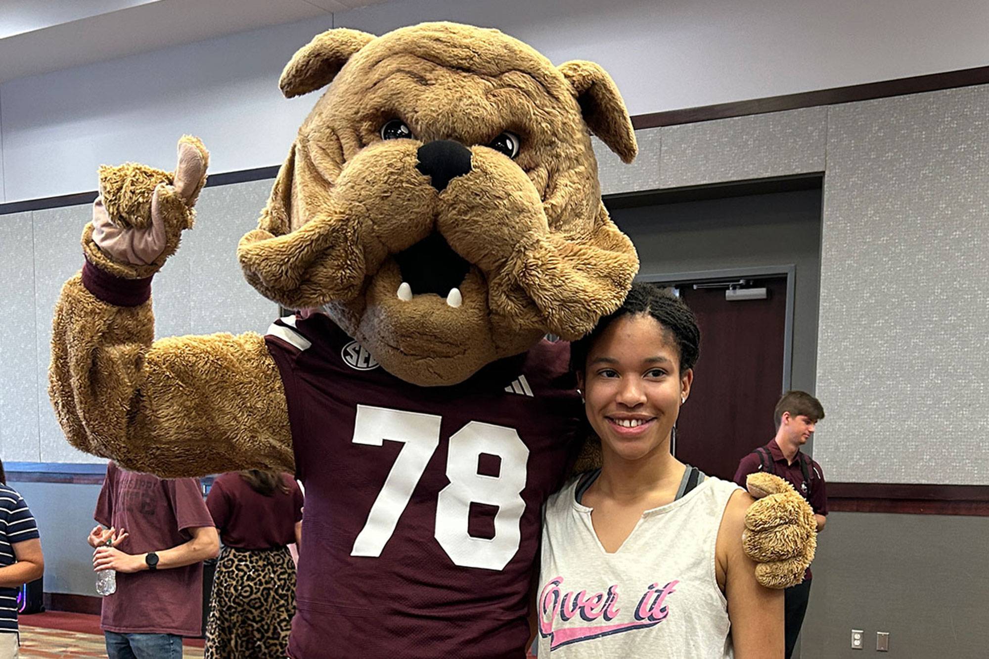 A bulldog mascot points up while wrapping an arm around a smiling teenager