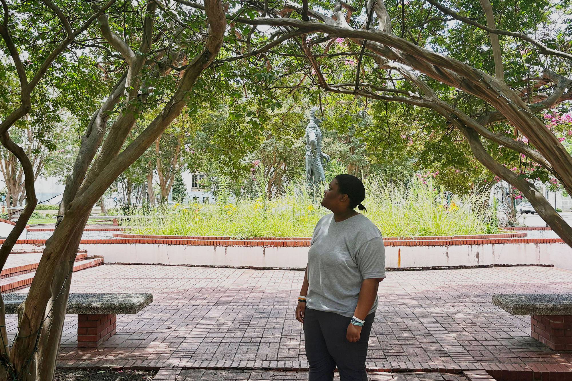 Lula Davis looks at the leaves of crepe myrtles that are arranged in an arc.