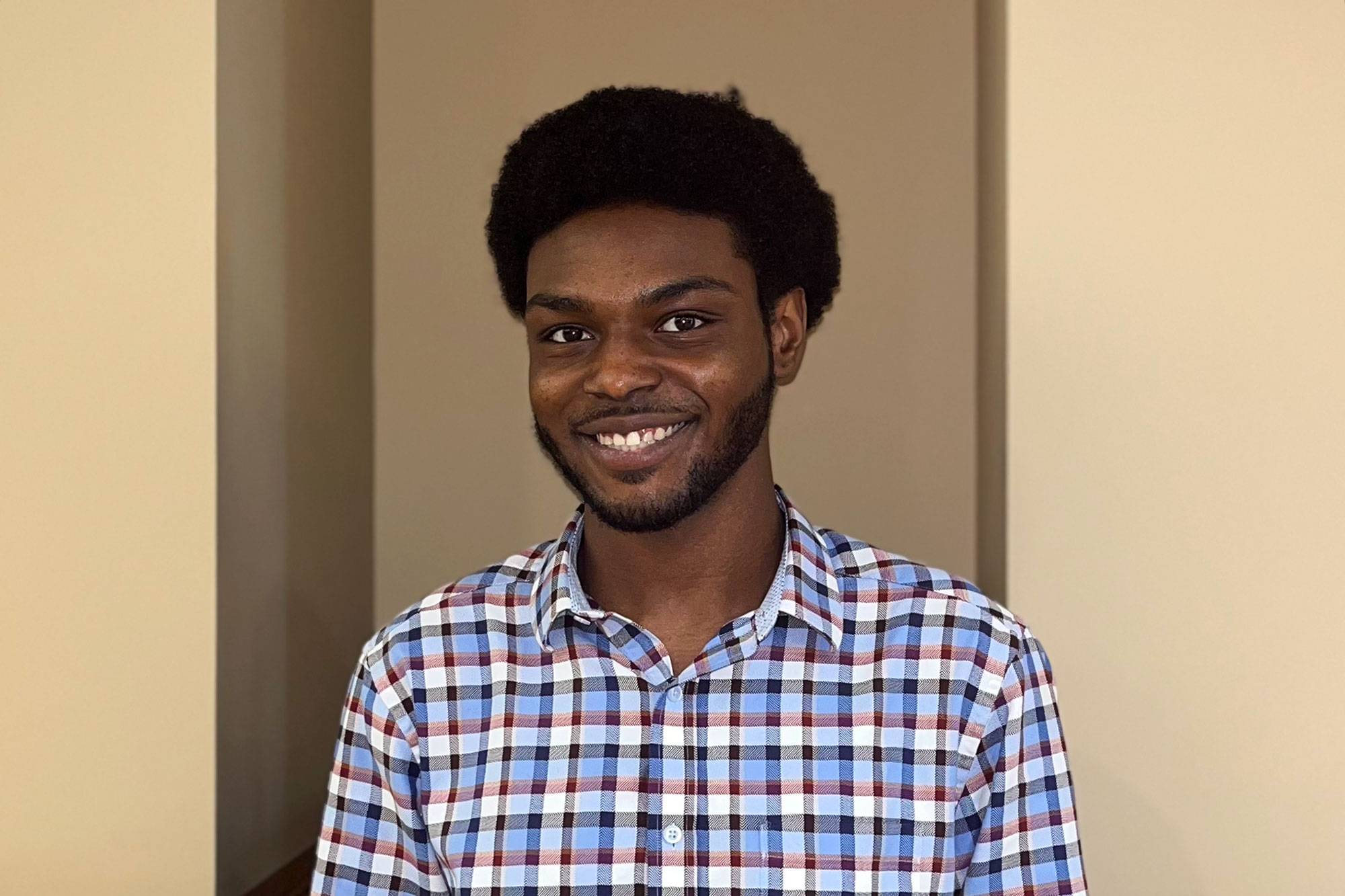 A young man in a blue and white checkered shirt smiles for the camera