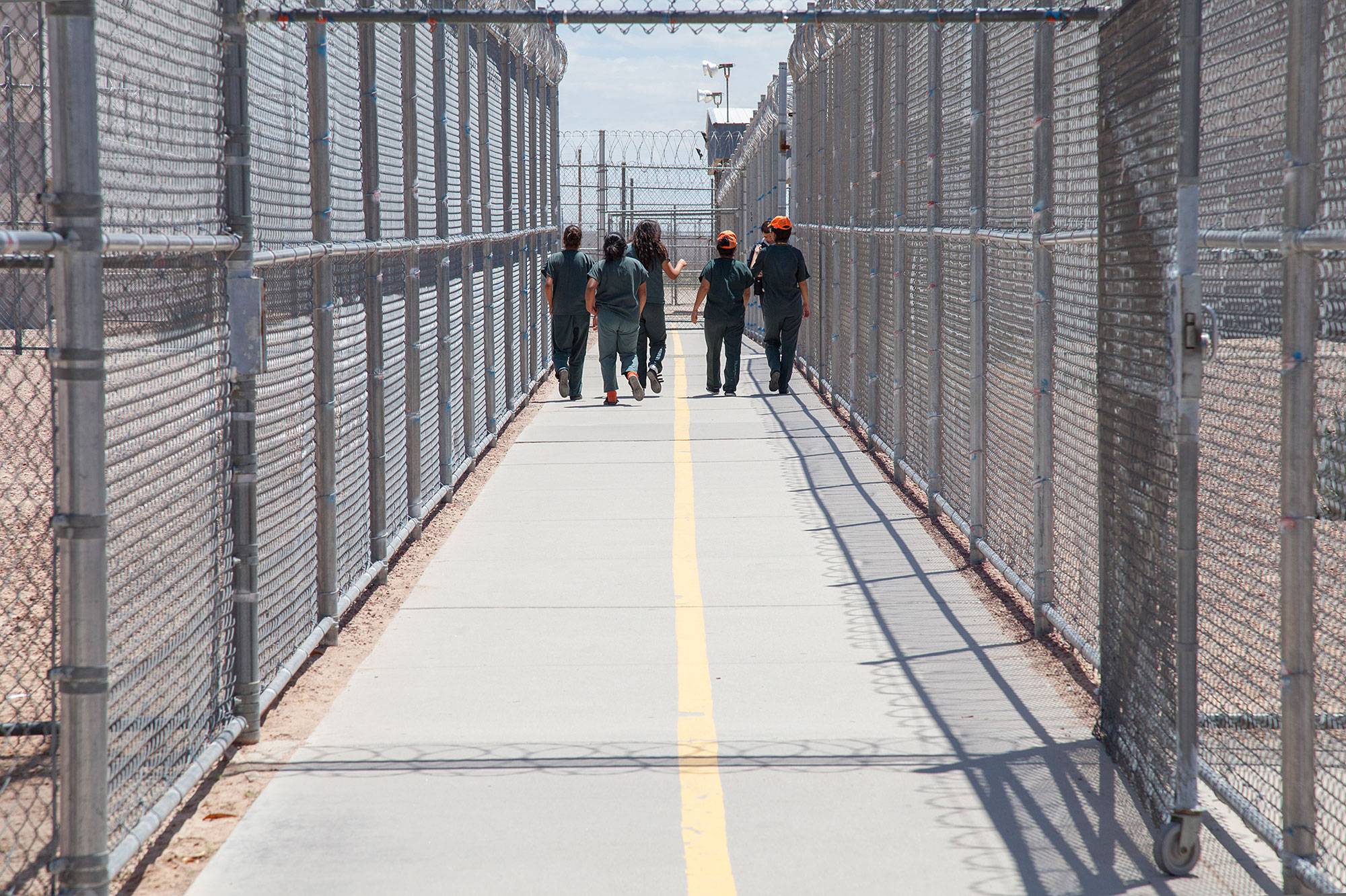 People in matching jumpers walking down a fenced path in a detention facility