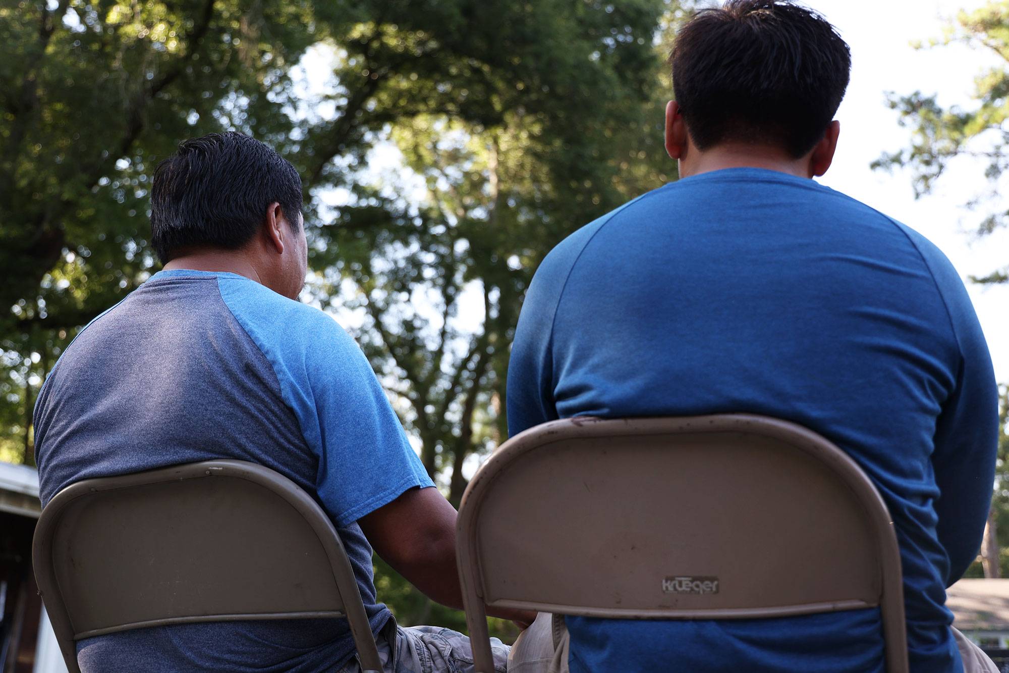 A view from behind two seated men wearing blue shirts