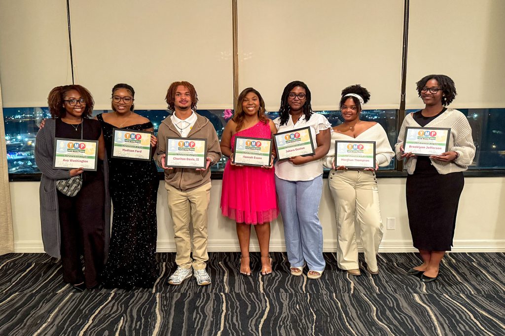Seven teens lined up by a window, each holding up a certificate